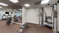 The fitness center at 2218 Benchley Ct. in Manchester, NJ offers a comprehensive exercise facility designed to accommodate a wide range of workout routines. The space is laid out across a single floor and features durable rubber flooring throughout, providing both comfort and safety during exercise. Illuminated by recessed flat-panel ceiling lights, the facility is evenly and brightly lit, contributing to an energizing atmosphere.

The cardio section is well-equipped with treadmills, elliptical trainers, and a stationary cycle, complemented by wall-mounted flat-screen TVs for entertainment during workouts. Multiple windows fitted with vertical blinds allow natural light to filter in while maintaining privacy. The strength training area includes a multi-functional cable machine, a weight bench, a dumbbell rack, and various selectorized machines suited for different muscle groups. Exercise balls add options for functional fitness training.

A large wall mirror in the strength area enhances the sense of space and allows users to monitor their form. The facility is equipped with clearly marked emergency exits and a fire extinguisher, ensuring a safe environment. The clean, neutral-toned walls and organized layout make this fitness center a practical and functional space for residents seeking convenient access to quality exercise amenities.