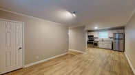 This single-floor unit offers a practical and well-appointed layout designed for comfortable everyday living. The open-concept living and dining area flows seamlessly into the kitchen, creating a connected, functional space. Light wood-look luxury vinyl plank flooring runs throughout the main living areas, complementing the warm neutral wall tones and crisp white crown molding and baseboards that frame each room. A textured ceiling adds subtle character overhead, while track lighting provides focused illumination in the main living space.

The kitchen is equipped with stainless steel appliances, including a range with overhead microwave, and features white cabinetry paired with granite-look countertops. A window above the sink brings in natural light, and a washer is conveniently housed within the kitchen area, adding in-unit laundry functionality.

The two bedrooms offer distinct finishes. One bedroom features medium-tone wood-look plank flooring, a window for natural light, and clean crown molding details. The second bedroom is carpeted, includes a ceiling fan with light fixture, a wall-mounted AC unit, and a window with outdoor views.

The full bathroom includes a tub-shower combination, a granite-top vanity with gray cabinetry, wood-look tile flooring, and brushed nickel fixtures, presenting a clean and updated aesthetic throughout.