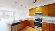 This single-floor residence offers a thoughtfully designed layout that balances functionality and comfort. The kitchen serves as a central highlight, featuring warm honey-toned cabinetry, granite countertops, and a full suite of stainless steel appliances, including an electric range, built-in microwave, and dishwasher. Three pendant lights hang above the peninsula, adding a refined touch while illuminating the workspace. The kitchen flows naturally into an open living and dining area finished with warm hardwood-style flooring, creating a bright and cohesive common space.

A large sliding glass door in the living area opens to a private balcony, offering elevated views of surrounding greenery and filling the room with abundant natural light. The bedrooms are carpeted for comfort; the primary bedroom includes a dedicated walk-in closet with built-in shelving and direct access to a bathroom with a tiled shower. A second bathroom features a full soaking tub with a tiled surround. An additional bedroom receives natural light through a window with blinds. Neutral wall tones throughout contribute to a clean, move-in-ready atmosphere.
