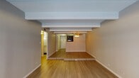 This single-floor residence is defined by a consistent architectural character, highlighted by exposed structural beams across textured ceilings that add depth and visual interest to each room. Wood-style flooring flows through the main living areas, complemented by plush carpeting in the bedrooms, creating a warm and comfortable atmosphere throughout.

The open living and dining area is generously proportioned, featuring a subtle stepped platform detail that distinguishes the two zones. A sliding glass door with vertical blinds opens to an outdoor area, allowing natural light to fill the space. A ceiling fan with a light fixture adds a functional decorative touch.

The galley-style kitchen is thoughtfully designed with dark espresso cabinetry, granite-look countertops, dark subway tile backsplash, and black appliances, including a range and refrigerator. Ample upper and lower cabinet storage lines both sides of the kitchen, maximizing functionality.

The bedroom offers carpeted flooring, exposed beam ceiling details, and access to a walk-in closet. The bathroom features a granite-topped vanity with white cabinetry, a wall sconce, a large mirror, and a separate shower-tub combination. A hallway with a louvered door provides additional storage. The overall ambiance is clean, neutral, and move-in ready.