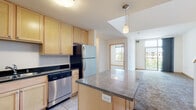This two-floor residential unit offers a functional and well-designed layout across both levels. The kitchen serves as a central highlight, featuring light maple cabinetry, dark granite countertops, a central island with additional counter space, and a full suite of stainless steel appliances including a refrigerator, dishwasher, microwave, and range. Large format tile flooring runs throughout the kitchen, providing a clean and durable surface. Pendant lighting above the island adds a finishing touch to the space.

The living areas transition to plush carpeting and are bathed in natural light courtesy of generously sized windows that frame views of the surrounding urban environment. The open flow between the kitchen and living spaces creates a cohesive, connected feel throughout the main floor.

The bathrooms are finished with tile flooring and include a full tub-and-shower combination, complemented by a vanity with granite countertop and maple cabinetry in at least one of the bathrooms. Bedrooms are carpeted and feature built-in closets with wire shelving systems for organized storage.

The second floor provides additional living space, also carpeted, with a window offering outside views. A staircase connects the two levels, and the overall layout—as visible in the dollhouse view—presents a spacious, multi-room configuration suitable for comfortable everyday living.