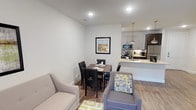This single-floor residence in Frisco presents a thoughtfully designed open-concept layout that seamlessly connects the living, dining, and kitchen areas. The kitchen is a standout feature, equipped with stainless steel appliances including a refrigerator, gas range, and built-in microwave. Dark espresso and light gray cabinetry create a striking two-tone contrast, complemented by granite countertops, a mosaic tile backsplash, and a peninsula with an undermount sink and pendant lighting overhead. Wood-look flooring flows throughout the main living areas, adding warmth and continuity to the space.

The dining area comfortably accommodates a four-person table, while the living space offers room for seating arrangements alongside framed artwork. The bedroom features plush carpeting, a ceiling fan, and a window providing natural light. A generously sized walk-in closet with dual hanging rods and shelving provides ample storage. The full bathroom includes wood-look flooring, a granite-topped vanity with storage cabinetry, and a soaking tub with tiled surround. Clean white walls and recessed lighting throughout contribute to a bright, modern ambiance.