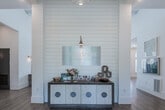 The Retreat at Bright Farms clubhouse is a thoughtfully designed single-story community facility that blends coastal-inspired aesthetics with modern functionality. The entrance foyer sets a polished tone with soaring ceilings, a shiplap accent wall, and a prominently displayed branded sign above a stylish console table, immediately establishing a welcoming atmosphere.

The open-plan interior flows naturally from the entry into a spacious lounge area, where white sofas with navy accent pillows surround a glass coffee table, anchored by a shiplap-clad fireplace wall with a mounted television. Warm light wood flooring extends throughout, complementing the crisp white walls and brass sconce lighting. Curated artwork and decorative furnishings add refined detail throughout.

A well-equipped kitchenette offers granite countertops, a double sink, under-counter refrigeration, and a large wall-mounted television, serving as a practical amenity hub. A private office with tall ceilings and an abundance of natural light from oversized windows provides a dedicated workspace.

A dramatic garage-style door opens the lounge directly to an expansive outdoor patio, where lounge chairs surround a resort-style pool—seamlessly connecting interior comfort with outdoor recreation. The overall ambiance is bright, airy, and inviting.