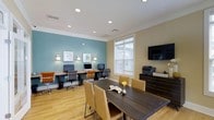 This single-floor business center is thoughtfully designed to accommodate a range of professional needs. The space features a dual-tone color scheme, with a calming teal accent wall contrasting against warm beige walls, creating an environment that is both focused and inviting. Recessed ceiling lighting ensures consistent, even illumination throughout.

Along one wall, a built-in granite-topped workstation provides multiple computer terminals, each equipped with monitors, ergonomic rolling chairs, and individual wall-mounted sconces for task lighting. A printer and additional office equipment are conveniently housed on a dark wood credenza nearby, alongside a wall-mounted flat-screen television.

At the center of the room, a dark wood rectangular conference table surrounded by cushioned tan chairs serves as an ideal space for meetings or collaborative work. Natural light filters in through a large window fitted with white blinds, adding brightness and an open feel to the room.

Light hardwood flooring ties the space together, complementing both the furniture and wall colors. Overall, the business center delivers a clean, professional atmosphere well-suited for work and productivity.