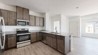 This single-floor unit showcases a cohesive modern design carried consistently throughout its rooms. The kitchen serves as a central highlight, featuring rich dark-stained cabinetry paired with granite countertops and a peninsula that includes a double-basin sink with a pull-down faucet. Stainless steel appliances—including an electric range, built-in microwave, dishwasher, and refrigerator—complete the well-equipped cooking space. Light wood-look luxury vinyl plank flooring extends through the kitchen and living areas, creating a clean, contemporary aesthetic against the crisp white walls and textured ceiling.

The bedrooms are finished with neutral-toned carpet and framed by large sliding windows that bring in natural light and offer views of the surrounding neighborhood. The rooms are generously proportioned, providing ample space for furnishings.

Both bathrooms continue the design language of the kitchen, featuring matching dark cabinetry with brushed nickel hardware, granite vanity countertops, and large rectangular mirrors. One bathroom includes a full tub-and-shower combination, while the other features a walk-in shower with a glass enclosure. Tile flooring completes each bathroom. A stacked laundry area is also visible in the floor plan layout, adding practical functionality to the unit.