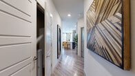 This thoughtfully designed 2-bedroom, 2-bathroom residence offers a cohesive modern aesthetic across its single floor. The entryway hallway features light wood-style flooring, recessed lighting, and striking geometric wall art, setting an inviting tone throughout. The open-concept kitchen is a standout, boasting dark wood cabinetry, stainless steel appliances, a subway tile backsplash, and a generous stone-topped island with bar seating, complemented by elegant pendant lighting. The adjacent dining area is bathed in natural light from a wraparound bank of windows dressed with sheer linen curtains and horizontal blinds. The living room continues the bright, airy feel with large windows offering outdoor views and warm, neutral tones. Both bedrooms feature plush carpeting, natural light from well-placed windows, and ample closet storage. The primary bedroom is generously proportioned and connects to a well-finished bathroom with dark wood vanity cabinetry, granite countertops, an undermount sink, a large mirror, and a walk-in shower. A dedicated hallway provides convenient access to the bedrooms and additional closets, ensuring efficient use of space throughout this well-organized and stylish residence.