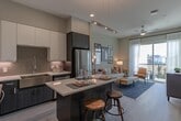 Located at 401 W 25th St in Houston, TX, this single-floor residence offers a well-designed open-concept layout that seamlessly connects the kitchen, dining, and living areas. The kitchen is a standout feature, boasting two-tone cabinetry with dark lower cabinets and crisp white upper cabinets, a herringbone tile backsplash, stainless steel appliances, a farmhouse-style sink, and a generous island with quartz countertops and bar seating — ideal for both cooking and entertaining. The adjoining living area is bright and inviting, with light wood-style flooring, recessed lighting, and ample wall space for art display. The bedroom is a comfortable retreat, featuring plush carpeting, a ceiling fan, and a large window that fills the room with natural light. The bathroom is finished with large-format tile flooring, dark cabinetry paired with a quartz vanity top, and a lighted mirror. A spacious walk-in closet with built-in shelving and hanging rods provides excellent storage. Throughout the residence, neutral tones and contemporary finishes create a cohesive, modern aesthetic that balances style with everyday functionality.