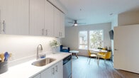 This single-floor residence offers a well-designed layout that balances functionality and modern style. The kitchen is outfitted with white shaker-style cabinetry featuring brushed nickel hardware, white quartz countertops, a stainless steel sink, and a full suite of stainless steel appliances, including a refrigerator, range, microwave, and dishwasher. An in-unit stacked washer and dryer is also conveniently located near the entryway. The kitchen flows naturally into the open living and dining area, which is brightened by large windows framing views of surrounding greenery. A ceiling fan with integrated lighting serves both the living space and the dining area. The living room provides a comfortable, versatile setting with wood-look flooring that extends throughout the unit. Two bedrooms are present; one features large windows with leafy treetop views and a sliding mirrored closet, while the other is served by its own set of windows and a ceiling fan. The bathroom includes a tub-shower combination, a white vanity with ample cabinet storage, a large mirror, and wood-look flooring, maintaining the clean, cohesive aesthetic found throughout the rest of the space.