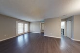 This single-story space offers a well-organized layout with a neutral color palette of warm gray tones throughout. The open living area is anchored by rich, dark hardwood-style flooring that extends through the main living and dining spaces, complemented by textured ceilings and clean white baseboards. French doors in the living room invite natural light and provide outdoor access, enhancing the sense of openness.

The dining area is distinguished by an elegant chandelier, adding a refined touch to the space, and connects directly to the galley-style kitchen. The kitchen is well-appointed with white shaker cabinets, dark countertops, a white subway tile backsplash, and a full suite of stainless steel appliances including a refrigerator, dishwasher, and range. Light-toned flooring and recessed lighting complete the functional workspace.

The bedrooms feature plush carpeting, ceiling fans, and windows with blinds that allow for natural light. The bathroom is finished with a white vanity cabinet, dark countertop, a large mirror with contemporary lighting, and wood-style flooring. A dedicated entry area with a private door provides a practical and clearly defined entryway into the unit.