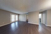 This single-story space offers a well-organized layout with a neutral color palette of warm gray tones throughout. The open living area is anchored by rich, dark hardwood-style flooring that extends through the main living and dining spaces, complemented by textured ceilings and clean white baseboards. French doors in the living room invite natural light and provide outdoor access, enhancing the sense of openness.

The dining area is distinguished by an elegant chandelier, adding a refined touch to the space, and connects directly to the galley-style kitchen. The kitchen is well-appointed with white shaker cabinets, dark countertops, a white subway tile backsplash, and a full suite of stainless steel appliances including a refrigerator, dishwasher, and range. Light-toned flooring and recessed lighting complete the functional workspace.

The bedrooms feature plush carpeting, ceiling fans, and windows with blinds that allow for natural light. The bathroom is finished with a white vanity cabinet, dark countertop, a large mirror with contemporary lighting, and wood-style flooring. A dedicated entry area with a private door provides a practical and clearly defined entryway into the unit.