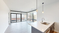 This contemporary apartment in Milwaukee offers a thoughtfully designed living space of 870 square feet. The single-floor layout comprises three bedrooms, including a spacious 170 square foot primary bedroom, and two well-appointed bathrooms. The heart of the home is an open-concept living area that seamlessly integrates with a sleek, modern kitchen. Large windows flood the space with natural light, creating an airy and inviting atmosphere.

The kitchen boasts a stylish design with a contrasting color scheme, featuring white upper cabinets and darker lower cabinets. Stainless steel appliances, including a refrigerator and built-in microwave, complement the clean lines of the space. A generous island with a white countertop provides additional workspace and casual dining options.

Bedrooms are carpeted for comfort, with the primary bedroom offering ample space for a king-sized bed and additional furniture. Bathrooms feature modern fixtures, with at least one including a glass-enclosed shower and elegant tile work. The apartment also includes a closet with wire shelving for organized storage.

Throughout the space, neutral tones dominate, creating a blank canvas for personal decorating styles. The combination of carpet in bedrooms and wood-look flooring in living areas adds warmth and practicality. Modern lighting fixtures, including pendant lights in the kitchen, enhance the contemporary feel of the apartment.