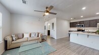 Located at 1603 W Walnut St in Rogers, Arkansas, this single-story unit offers a thoughtfully designed open-concept floor plan that seamlessly connects the living, dining, and kitchen areas. Light wood-look flooring runs throughout, complementing the clean, neutral color palette and creating a bright, cohesive atmosphere.

The living area is generously proportioned, featuring a ceiling fan with light fixture and large windows dressed with horizontal blinds that allow ample natural light to fill the space. The kitchen is a standout feature, showcasing dark espresso cabinetry, crisp white quartz countertops, and a large peninsula island with an undermount sink — ideal for both meal preparation and casual dining. A full suite of stainless steel appliances, including a refrigerator, range, over-the-range microwave, and dishwasher, completes the kitchen.

The unit includes two well-sized bedrooms, each equipped with ceiling fans and windows that bring in natural light. Both rooms offer closet storage and maintain the consistent wood-look flooring found throughout the home. The bathroom features dark cabinetry with white countertops, a full tub-shower combination, and a large mirror, maintaining the modern aesthetic carried throughout the space. The overall design is clean, contemporary, and move-in ready.
