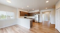 This single-floor residence offers a thoughtfully designed layout with two bedrooms, two bathrooms, and a connected kitchen and living area. The open-concept kitchen is a standout feature, showcasing rich walnut-toned cabinetry that extends to the ceiling, white quartz countertops, a peninsula with a built-in sink, and a full suite of stainless steel appliances including a refrigerator, range, and microwave. Light wood-style flooring runs throughout the main living areas, lending warmth and continuity to the space. A hallway connects the main living area to the private quarters, offering a clear separation between shared and personal spaces. The bedrooms are carpeted for comfort and feature large windows with blinds that invite plentiful natural light and outdoor views of the surrounding neighborhood. One bedroom includes corner windows on two walls, maximizing both light and views. The two bathrooms are finished with tile flooring, wood-toned vanities with white countertops, large mirrors, and grab bars, reflecting both style and accessibility. One bathroom features a shower-tub combination with a window above for natural light. The overall aesthetic is clean, modern, and neutral, creating a move-in ready environment with a bright and comfortable ambiance throughout.