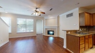 This two-story home showcases a thoughtfully designed layout that balances open communal spaces with functional private areas. The main living area is anchored by rich hardwood flooring and a classic tiled fireplace framed by a white mantel, complemented by crown molding and a ceiling fan with a light fixture. Natural light filters in through slatted blinds, and an arched doorway adds an elegant architectural detail connecting adjacent spaces.

The open-concept design seamlessly links the living area to the kitchen, which is well-appointed with warm oak cabinetry, granite countertops featuring earth-toned veining, and a dark stone tile backsplash. A central island provides additional prep space, while stainless steel appliances—including a refrigerator, range, and over-the-range microwave—complete the kitchen. Tile flooring runs throughout this area, transitioning to hardwood in the adjoining dining and living spaces.

The primary bathroom includes a dual-sink vanity with oak cabinetry and a separate glass-enclosed shower. A secondary bathroom offers a tiled tub-shower combination with classic white tile surround. Upstairs, the spacious primary bedroom features plush carpeting, crown molding, abundant natural light from multiple windows, a walk-in closet, and sliding door access.
