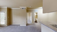 This single-story, one-bedroom, one-bathroom unit offers a functional and efficiently designed layout. The open-concept living room and kitchen area serve as the heart of the unit, with the living space featuring neutral-toned carpet, crown molding, and elevated ceilings that contribute to an airy feel. A front entry door and a secondary door with an adjacent window allow for natural light. The kitchen is configured in a galley style, equipped with stainless steel appliances including a refrigerator and range, white cabinetry, laminate countertops, a single-basin sink, and durable wood-look flooring.

The bedroom is a comfortable, carpeted space featuring a ceiling fan with light fixture, a built-in desk with shelving, and a window providing natural light. An attached walk-in closet offers wire shelving and hanging rods for ample storage. The bathroom includes a soaking tub and shower combination with white tile surround accented by a decorative tile border in neutral tones. Additional utility space provides practical functionality. Warm beige tones are consistent throughout, creating a cohesive and neutral aesthetic.