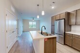 Located at 964 Constitution Blvd in Rock Hill, SC, this one-bedroom, one-bathroom unit offers a thoughtfully designed open-concept floor plan that maximizes its comfortable footprint. The kitchen and living area flow seamlessly together, anchored by a central island with a double-basin sink, matte black faucet, and light countertops — ideal for both meal prep and casual dining. The kitchen is well-equipped with warm-toned wood cabinetry, a full suite of stainless steel appliances including a refrigerator, range, and over-the-range microwave, and durable light-wood-style flooring that extends throughout the main living areas. Pendant lighting above the island adds a modern touch, while a ceiling fan in the living area promotes airflow and comfort. Natural light filters in through a window at the far end of the living space, offering views of the surrounding area. The spacious primary bedroom features plush carpeting, a ceiling fan, and direct access to a dedicated closet. The full bathroom is clean and functional, complete with a single-vanity with wood cabinetry, a large mirror, and a tub-shower combination. Throughout the unit, neutral tones and clean finishes create a bright, move-in-ready atmosphere.