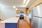 Located at 8 S Sixth St in Council Bluffs, Iowa, this two-bedroom, two-bathroom single-floor unit blends industrial character with modern updates. The open kitchen is a standout feature, showcasing warm wood cabinetry, white subway tile backsplash, stainless steel appliances, and a distinctive navy blue island topped with a white quartz countertop. Globe pendant lights hang above, complemented by a skylight that bathes the space in natural light. Exposed brick accents add architectural charm throughout. Terracotta tile flooring flows through the kitchen and main living area, where large windows allow ample daylight and views of the brick exterior wall, reinforcing the building's industrial aesthetic. A long, well-lit hallway with soft carpeting connects the main living space to the private quarters. Both bedrooms are carpeted, bright, and generously sized, each with access to a closet. The primary bedroom features elevated ceilings, a dedicated closet, and direct access to a full bathroom equipped with warm wood vanity cabinetry and a tub-shower combo. The second full bathroom mirrors this clean, functional design. The layout is efficient and practical, offering comfortable living within a thoughtfully designed, character-rich space.