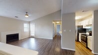This single-floor residence offers a thoughtfully designed open layout highlighted by vaulted ceilings that lend a sense of spaciousness to the main living areas. Wide-plank wood-look flooring runs consistently throughout the unit, providing a cohesive and clean aesthetic. The living room serves as a central gathering space, featuring a classic brick-surround fireplace flanked by windows fitted with blinds that allow for adjustable natural light. A ceiling fan with integrated lighting adds both comfort and functionality.

The kitchen is designed for efficiency, featuring a galley-style layout with white shaker cabinetry, a mosaic tile backsplash, stainless steel appliances including a refrigerator and range, and light countertops. A pass-through bar with seating connects the kitchen to the living and dining areas, promoting an open flow. A stacked in-unit washer and dryer is conveniently located within the kitchen space.

The bedrooms are well-proportioned, each offering hardwood-style flooring, natural light from windows with blinds, and closet storage. The bathroom features a white vanity with modern hardware, a mirror, and a toilet, with access to an adjacent closet for additional storage. Textured ceilings are present throughout, and neutral wall tones create a calm, versatile backdrop across all rooms.