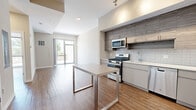 Located at 900 Pacific St in Stamford, Connecticut, this two-bedroom, one-bathroom residence offers a well-organized single-floor layout with a clean, contemporary aesthetic throughout. Warm hardwood-style flooring runs continuously across the living spaces, lending a sense of cohesion and comfort to the home.

The combined kitchen and living area forms the heart of the residence. The kitchen is outfitted with stainless steel appliances — including a gas range, microwave, dishwasher, and refrigerator — complemented by textured gray cabinetry, a white tile backsplash, and a central island with a sleek white countertop ideal for casual dining or meal prep. Track lighting above the kitchen enhances functionality.

The living area flows naturally from the kitchen, offering an open, airy feel with neutral walls and generous natural light. Large sliding glass doors lead directly to an outdoor terrace, bringing in views of surrounding greenery and providing seamless indoor-outdoor connectivity.

The primary bedroom is a comfortably proportioned retreat, featuring a floor-to-ceiling sliding glass door that opens to the terrace, flooding the space with sunlight. The second bedroom is well-sized with neutral tones and practical layout. The bathroom is finished with white subway tile surrounding a full soaking tub and shower, paired with hardwood-style flooring and clean modern fixtures.