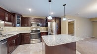 Located at 1411 Adams St in Mankato, MN, this well-appointed 2-bedroom, 2.5-bathroom residence offers a thoughtfully designed single-floor layout with a generous amount of living space. The open-concept kitchen and living room serve as the heart of the home, where the kitchen impresses with rich dark wood cabinetry, granite countertops, a large center island with pendant lighting, and a full suite of stainless steel appliances including a range, microwave, dishwasher, and French door refrigerator. Tile flooring completes the kitchen's polished look. The spacious living room features plush wall-to-wall carpeting, warm neutral tones, and large windows and sliding glass doors that flood the space with natural light and provide access to a private balcony. Both bedrooms are generously sized, carpeted, and equipped with ceiling fans. The primary bedroom includes an en-suite bathroom featuring a wide vanity with quartz countertops, dark wood cabinetry, and a walk-in glass-door shower. Two additional closets, an in-unit laundry room, and a utility room round out the functional layout. With 2.5 bathrooms in total, this residence is well-suited for both comfort and everyday convenience.