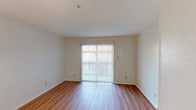 This two-story, 2-bedroom, 1.5-bathroom residence offers a practical and comfortable layout spread across two well-defined levels. The main floor features a galley-style kitchen equipped with warm wood-tone cabinetry extending floor to ceiling, white countertops, a stainless steel range, dishwasher, and a sink. Light wood-style flooring runs throughout the main living areas, lending a clean, cohesive look. The adjoining dining area is brightened by a pendant light fixture, and the spacious living room benefits from generous natural light provided by a large sliding glass door fitted with vertical blinds, offering access to the outdoors. A staircase with a classic baluster railing connects the two floors. Upstairs, both bedrooms are carpeted and feature neutral walls, natural window light, and closets with hanging rods for storage. The layout positions the bedrooms off a shared upper hallway. The full bathroom includes a tiled tub-shower combination, toilet, and tile flooring, presented in an all-white palette. A half bath serves the lower level. Throughout, the design is straightforward and functional, with a neutral color scheme that provides a versatile backdrop suitable for a variety of furnishing styles.