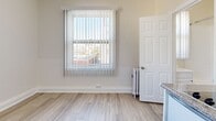 Located at 729 S Union Ave in the heart of Los Angeles, CA, this single-room unit offers a clean, functional layout designed to maximize every inch of available space. The interior is finished with light wood-look plank flooring throughout, creating a bright and cohesive aesthetic that complements the neutral white walls and crisp white baseboards.

The kitchenette area is efficiently arranged along one wall and features white upper cabinetry with a subway tile backsplash, a granite-look countertop with an integrated sink, a compact cooktop, and a mini refrigerator — providing all the essential amenities in a streamlined footprint.

Multiple windows fitted with vertical blinds are positioned throughout the room, allowing natural light to filter in while offering privacy control. Views from the windows look out toward the surrounding Los Angeles neighborhood streetscape. A cast iron radiator is visible near one window, indicating a traditional heating system.

The entry door is centrally located and painted white, contributing to the room's clean, uniform finish. The textured ceiling adds a subtle architectural detail overhead. The overall ambiance is minimal, bright, and move-in ready, making this a practical urban living space in a well-connected Los Angeles location.