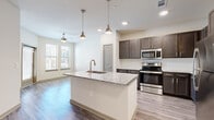Located at 651 E Finley Blvd in Anna, TX, this one-bedroom, one-bathroom unit offers a thoughtfully designed open-concept layout across a single floor. The kitchen serves as the centerpiece of the living area, showcasing a large island with a granite countertop, an undermount sink, and stylish pendant lighting overhead. Dark-toned cabinetry with brushed hardware pairs with a subway tile backsplash and a full suite of stainless steel appliances, including a range, microwave, and refrigerator. Wood-style plank flooring flows throughout the main living and kitchen areas, complementing the bright, neutral color palette of the walls. Natural light filters in through windows that overlook the surrounding community. The living area transitions smoothly from the kitchen, creating an inviting, cohesive space. The bedroom offers a comfortable footprint with plush carpeting, a ceiling fan, and dual windows that bring in ample daylight. A dedicated closet provides convenient storage. The bathroom mirrors the kitchen's finishes, featuring a granite-topped vanity with dark cabinetry, a brushed nickel faucet, and a large mirror. A hallway connects the rooms, contributing to the unit's efficient and functional flow throughout.