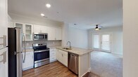 This single-story residence is designed with an open-concept layout that seamlessly connects the kitchen and living area, creating a cohesive and functional living space. The kitchen is a standout feature, appointed with crisp white shaker-style cabinetry, light granite countertops, a subway tile backsplash, and a full suite of stainless steel appliances including a range, microwave, refrigerator, and dishwasher. A peninsula with an undermount sink and additional counter space extends into the main living area, providing both a practical workspace and a natural dividing point between the kitchen and living room. Hardwood-style flooring runs throughout the kitchen and entry areas, while plush carpeting carries through the living room and bedroom. The living area benefits from natural light through a set of glass-paneled doors and is fitted with a ceiling fan overhead. Crown molding and recessed lighting add refined detail to the shared spaces. The bedroom is a calm, neutral retreat featuring carpeted flooring and a reach-in closet with built-in shelving for organized storage. The bathroom is finished with a granite-topped vanity, hardwood-style flooring, a tub-shower combination with tiled surround, and a window that introduces natural light.