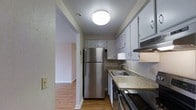 This single-floor, 1-bedroom, 1-bathroom residence offers a practical and comfortable layout designed to maximize everyday living. The galley-style kitchen is a standout feature, outfitted with stainless steel appliances including a full-size refrigerator, an electric range, and a built-in microwave hood. White upper and lower cabinetry provides ample storage, while the granite-look countertops and double-basin sink add a clean, functional aesthetic. Recessed ceiling lighting brightens the kitchen space efficiently. The kitchen opens directly into the living area, creating a natural flow between the two spaces. Warm hardwood-style flooring runs throughout, lending the home a cohesive and inviting character. Neutral wall tones complement the light-toned floors and white trim, creating a bright and airy atmosphere. The layout connects the main living spaces in a straightforward, easy-to-navigate manner, making the home feel open and accessible. Overall, this residence provides a well-appointed, move-in-ready living environment suited for comfortable single-occupant or couple living.