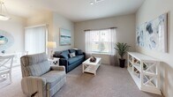 Located at 504 Coventry Ln in Salisbury, Maryland, this single-floor residence offers a thoughtfully designed layout with a warm, coastal-inspired aesthetic throughout. The living room is a welcoming space featuring plush carpeting, large windows with sheer curtains that allow natural light to fill the room, and tasteful décor including a seascape painting that reinforces the relaxed ambiance. A dining area flows seamlessly from the living space, anchored by a pendant light fixture. The kitchen is well-equipped with rich dark-wood cabinetry, granite countertops, light hardwood-style flooring, a center island for additional prep space, and a full suite of black appliances including a refrigerator, range, and over-the-range microwave. Ample storage is provided by a large pantry closet. The primary bedroom is a serene retreat with carpeted floors, a sizable window, and a calming neutral palette. A second bedroom offers generous space and natural light, ideal for multiple uses. Both bathrooms mirror the kitchen's design language, featuring granite-topped vanities with dark wood cabinetry and light hardwood-style flooring. One bathroom includes a soaking tub with shower, while the other offers a walk-in shower configuration.