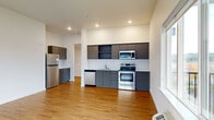 This thoughtfully designed 2-bedroom, 2-bathroom residence offers a functional and modern living experience across a single floor. The open-concept kitchen and living area serves as the heart of the home, featuring warm hardwood-style flooring, recessed lighting, and large windows that invite ample natural light and outdoor views of the surrounding neighborhood and greenery. The kitchen is outfitted with sleek gray cabinetry, a classic white subway tile backsplash, white quartz countertops, and a full suite of stainless steel appliances including a refrigerator, range, microwave, and dishwasher. A central hallway connects the living spaces to the private quarters, finished with the same hardwood-style flooring and recessed lighting for a cohesive feel. The spacious primary bedroom is carpeted for comfort and features a sliding closet and a window with neighborhood views. The second bedroom also features carpet and a window with outdoor scenery. Both bathrooms are identically appointed with a tub/shower combo, white vanity with quartz countertop, gray cabinetry, and hardwood-style flooring. A dedicated utility room and in-unit climate control round out this well-organized and move-in ready home.