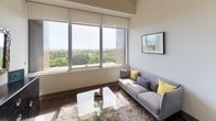 Located along the iconic South Michigan Avenue corridor in Chicago, this single-floor residence offers a thoughtfully designed layout with contemporary finishes throughout. The living area is a standout, anchored by a wide bank of floor-to-ceiling windows that flood the room with natural light and frame sweeping views of Grant Park and Lake Michigan beyond — a rare urban backdrop that brings the outdoors in. Dark hardwood-style flooring runs throughout, providing a warm contrast to the crisp white walls and light-toned furnishings.

The kitchen is efficiently designed with sleek wood-grain cabinetry extending to the upper walls, white countertops, and a full suite of stainless steel appliances including a refrigerator, dishwasher, built-in microwave, and smooth-top range — delivering both style and functionality in a compact footprint.

The bedroom is calm and understated, with generous wall space, high ceilings, and a clean, neutral palette that promotes rest and relaxation. The bathroom continues the modern aesthetic with a floating wood-toned vanity, white countertop, mirrored medicine cabinet, and a tub-shower combination accented by a patterned curtain, all set against light walls and dark flooring for a polished finish.