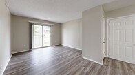 Located at 415 NE Delaware Ave in Ankeny, Iowa, this 2-bedroom, 1-bathroom unit offers a clean, modern aesthetic throughout its single-floor layout. Consistent light-toned vinyl plank flooring runs throughout the entire space, complementing the neutral beige walls and white trim found in every room.

The combined kitchen and living area forms the heart of the unit. The kitchen is well-appointed with white cabinetry, granite-style countertops, black appliances including a range, over-the-range microwave, dishwasher, and refrigerator, plus a ceiling-mounted track light. A peninsula provides additional counter space. The living area is bright and open, featuring a sliding glass door that leads to an outdoor patio and allows generous natural light to fill the room.

The primary bedroom offers a comfortable footprint with a double sliding-door closet and a window with outdoor views. The second bedroom is similarly finished with a window and a standard closet, maintaining the same neutral palette. A hallway connects the private areas of the unit.

The bathroom features a white vanity with a granite-topped sink, a full tub-shower combination, and matching vinyl flooring. Textured ceilings are present throughout, adding subtle architectural character to the otherwise clean, modern interior.
