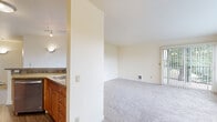 This single-floor residence offers a practical and comfortable layout designed for everyday living. The open living area is finished with plush carpeting and neutral cream-toned walls, creating a bright and versatile space. Large windows dressed with vertical blinds flood the room with natural light while framing serene views of surrounding greenery. A wall-mounted air conditioning unit and baseboard heating ensure year-round comfort.

The kitchen is efficiently arranged and features warm-toned wood cabinetry with stone-look countertops, stainless steel appliances including a refrigerator, electric range, and over-the-range microwave, and durable wood-look flooring. Track lighting overhead adds a functional and modern touch to the cooking space.

A partial wall separates the kitchen from the living area, providing a sense of definition while maintaining an open feel. The bathroom is accessed through a dedicated hallway and offers wood-look flooring, a single vanity with warm cabinetry, stone-look countertops, a large mirror, and polished chrome fixtures. The bedroom is generously proportioned, carpeted, and benefits from abundant natural light through a wide window overlooking lush trees, complemented by a baseboard heater for added comfort.