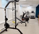 The Pelham Hall Gym is a compact yet comprehensive fitness center, maximizing its 490 square feet to offer a variety of exercise options. The space is thoughtfully designed with distinct zones for different workout styles. The gym features a cardio area equipped with modern treadmills and elliptical machines, each outfitted with digital displays for tracking performance. A strength training section includes a multi-functional power rack, free weights, and adjustable benches. The facility also incorporates cable machines and resistance equipment for versatile strength exercises. A dedicated area houses exercise balls and other functional training tools, adding variety to workout routines. The gym's design emphasizes cleanliness and organization, with mirrored walls enhancing the sense of space and allowing users to monitor their form. Bright, energy-efficient lighting illuminates the entire area, while large windows provide natural light and ventilation. The color scheme features a mix of neutral tones with accents of blue, creating a motivating yet calming atmosphere. Despite its modest size, the Pelham Hall Gym offers a well-rounded fitness experience suitable for various exercise preferences and skill levels.