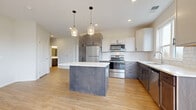 This well-designed single-floor residence combines modern finishes with a thoughtful, open layout. The centerpiece of the home is a spacious open-concept kitchen, showcasing a two-tone cabinet design with grey-toned lower cabinets and crisp white uppers, complemented by a classic white subway tile backsplash. A large central island with a white quartz countertop anchors the space, illuminated by stylish glass pendant lights. Stainless steel appliances, including a refrigerator, range, microwave, and dishwasher, complete the kitchen. Light wood-look flooring runs throughout the main living areas, creating a warm and cohesive aesthetic. The living area benefits from abundant natural light streaming through multiple windows, with direct access to a private balcony offering outdoor views. Bedrooms are generously proportioned, with plush carpeting, large windows framing scenic outdoor views, and ample closet space, including a walk-in closet with wire shelving. The bathroom features a dark-stained vanity with a white countertop, a large mirror, and clean, neutral finishes. A dedicated in-unit laundry room with a full-size washer and dryer adds everyday convenience. Throughout the residence, recessed lighting, clean white walls, and consistent modern hardware tie the design together seamlessly.