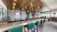 Located in the heart of Houston's vibrant Montrose neighborhood, this upscale amenity space delivers a refined, contemporary experience across a generously sized single-floor layout. The interior design blends bold textures and rich materials throughout, including striated wood-paneled ceilings, polished large-format tile flooring, and striking perforated decorative wall panels that add depth and visual interest.

The main lounge area features an elegant seating arrangement with tufted leather sofas, accent chairs, and curated artwork, all beneath a statement ceiling detail inlaid with a dramatic marbled panel. Recessed and pendant lighting—including eye-catching metallic globe fixtures—creates a warm, inviting ambiance. A dedicated bar area showcases a long counter with green velvet bar seating, wood-grain striped ceiling treatments, and multiple mounted displays, ideal for social gatherings.

A separate lounge zone with a billiards table and additional leather seating offers a more relaxed setting, while a kitchen and dining nook with iridescent tile backsplash and pendant lighting serves as a refined entertaining hub. Floor-to-ceiling sliding glass doors open to multiple wraparound outdoor terraces with glass-railed balconies, warm wood-clad ceilings, and sweeping views of the Houston skyline—making this space as impressive outside as it is within.