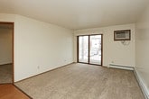 This single-floor residence offers a practical and comfortable layout with a cohesive design throughout. The kitchen is well-appointed with warm oak cabinetry, white appliances including a refrigerator, electric range, over-the-range microwave, and a dishwasher, all set atop light hardwood-style flooring. A chandelier overhead adds a touch of warmth to the space. The kitchen opens toward the living area, which features plush carpeting and a large sliding glass door that brings in natural light and provides outdoor views. Baseboard heating and a wall-mounted air conditioning unit ensure year-round climate comfort. Two bedrooms are carpeted and each equipped with a ceiling fan and windows that frame views of the surrounding greenery, contributing to a bright and airy feel. Baseboard heaters are present in both bedrooms for added comfort. The full bathroom is finished with hardwood-style flooring, a combined tub and shower with sliding glass doors, a toilet, and a dedicated storage closet. The overall ambiance of the space is clean, practical, and inviting, with a consistent use of neutral tones and natural wood accents that create a cohesive and welcoming atmosphere throughout.