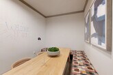 Located at 400 Southwest Pkwy in College Station, Texas, this compact private meeting room offers a focused and functional environment ideal for small group gatherings or collaborative sessions. The single-level space is efficiently laid out, making the most of its intimate footprint.

The room features crisp white walls accented by gray crown molding, lending a clean, professional aesthetic. A standout element is the full whiteboard wall, complete with a marker caddy, providing an interactive surface for brainstorming and presentations. Built-in bench seating upholstered in a warm, multicolored geometric fabric lines one side of the room, complemented by cushioned chairs positioned around a substantial light wood table. A decorative bowl of preserved moss serves as a natural centerpiece atop the table.

Two framed abstract artworks in blue and gray tones adorn one wall, adding a sophisticated artistic touch. A pass-through interior window connects the room to an adjacent office area, allowing for visibility while maintaining separation. A patterned area rug grounds the seating arrangement, adding texture and warmth to the space.

Overall, the room strikes a balance between practicality and polished design, making it a welcoming and well-equipped setting for meetings, consultations, or collaborative work.