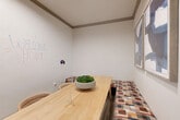 Located at 400 Southwest Pkwy in College Station, Texas, this compact private meeting room offers a focused and functional environment ideal for small group gatherings or collaborative sessions. The single-level space is efficiently laid out, making the most of its intimate footprint.

The room features crisp white walls accented by gray crown molding, lending a clean, professional aesthetic. A standout element is the full whiteboard wall, complete with a marker caddy, providing an interactive surface for brainstorming and presentations. Built-in bench seating upholstered in a warm, multicolored geometric fabric lines one side of the room, complemented by cushioned chairs positioned around a substantial light wood table. A decorative bowl of preserved moss serves as a natural centerpiece atop the table.

Two framed abstract artworks in blue and gray tones adorn one wall, adding a sophisticated artistic touch. A pass-through interior window connects the room to an adjacent office area, allowing for visibility while maintaining separation. A patterned area rug grounds the seating arrangement, adding texture and warmth to the space.

Overall, the room strikes a balance between practicality and polished design, making it a welcoming and well-equipped setting for meetings, consultations, or collaborative work.