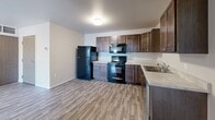 Located at 1410 Catron Blvd in Rapid City, South Dakota, this single-story, 3-bedroom, 2-bathroom home offers a practical and comfortable layout. The kitchen is a functional highlight, featuring rich dark-stained cabinetry, light countertops, a double-basin stainless steel sink, and black appliances including a range, microwave, and refrigerator, complemented by a stainless dishwasher. Wood-look luxury vinyl plank flooring runs throughout the kitchen and bathrooms, providing a clean, durable finish. The three bedrooms are carpeted in a neutral, soft-toned plush carpet and benefit from natural light through windows with horizontal blinds. The primary bedroom is a generous size and connects to one of the two bathrooms. The bathrooms feature the same wood-look flooring, with one showcasing a rich dark-wood vanity with a light countertop and mirror, and the other offering a full shower-tub combo with a curtain rod. Clean white walls and neutral tones throughout the home create a bright, move-in-ready atmosphere. The floor plan, visible in the dollhouse view, reflects a well-organized single-level layout that makes efficient use of the available space.