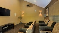 This intimate screening room is thoughtfully designed to deliver a true cinematic experience. The space features tiered rows of plush, oversized recliner chairs with built-in cup holders, arranged to ensure unobstructed sightlines for every seat. The seating is upholstered in a combination of rich, dark fabric and complementary light tones, creating a visually inviting and comfortable environment.

The vaulted ceiling adds a sense of openness and grandeur to the room, with a ceiling fan providing gentle air circulation. Warm, amber-toned wall sconces are mounted along the walls, casting a soft, ambient glow that enhances the cozy, theater-like atmosphere while keeping the space stylishly lit. The warm tan walls contribute to the room's inviting and relaxed ambiance.

Carpeted flooring in a subtle striped pattern adds texture underfoot and helps with acoustic performance, enhancing the overall viewing experience. A decorative potted bonsai-style tree in the corner adds a natural, organic touch, softening the space and providing a refined aesthetic accent. Recessed lighting in the ceiling offers additional illumination options. The overall design balances functionality with comfort, making this a well-appointed space ideal for private film screenings or media viewing gatherings.