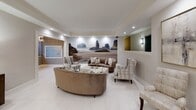 The lobby at 44 Hill St in Morristown, New Jersey presents a polished and sophisticated first impression. The space is finished with large-format white porcelain tile flooring that extends throughout, complemented by neutral warm-gray walls and crisp white crown molding that lend a clean, refined aesthetic.

The elevator vestibule features two elevator doors framed by classic white molding trim, flanked by wall sconces that provide warm accent lighting. A charcoal entry mat grounds the transition area, while a curved reception desk with a glass top anchors the entry point.

The adjoining lounge area serves as a comfortable gathering space, furnished with curved velvet sofas, plaid upholstered accent chairs, and a white marble-topped coffee table. A dramatic full-wall photographic mural depicting a coastal seascape serves as a striking focal point, adding depth and a serene ambiance to the room. Recessed lighting throughout keeps the space bright and inviting.

Decorative elements include framed abstract artwork, a sunburst mirror, a console cabinet with metallic hardware, and carefully curated accessories that elevate the overall design. A resident mailbox station is conveniently integrated into the lounge area. The layout flows seamlessly between the entry, elevator corridor, and seating zones, creating a lobby that is both functional and visually impressive.