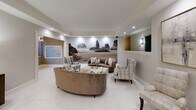 The lobby at 44 Hill St in Morristown, New Jersey presents a polished and sophisticated first impression. The space is finished with large-format white porcelain tile flooring that extends throughout, complemented by neutral warm-gray walls and crisp white crown molding that lend a clean, refined aesthetic.

The elevator vestibule features two elevator doors framed by classic white molding trim, flanked by wall sconces that provide warm accent lighting. A charcoal entry mat grounds the transition area, while a curved reception desk with a glass top anchors the entry point.

The adjoining lounge area serves as a comfortable gathering space, furnished with curved velvet sofas, plaid upholstered accent chairs, and a white marble-topped coffee table. A dramatic full-wall photographic mural depicting a coastal seascape serves as a striking focal point, adding depth and a serene ambiance to the room. Recessed lighting throughout keeps the space bright and inviting.

Decorative elements include framed abstract artwork, a sunburst mirror, a console cabinet with metallic hardware, and carefully curated accessories that elevate the overall design. A resident mailbox station is conveniently integrated into the lounge area. The layout flows seamlessly between the entry, elevator corridor, and seating zones, creating a lobby that is both functional and visually impressive.