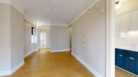 Located at 1222 SW Broadway in the heart of Portland, Oregon, this thoughtfully laid-out unit offers a well-organized single-floor plan comprising a living room, kitchen, bathroom, and two hallways. Light hardwood flooring runs throughout, lending warmth and continuity to each space.

The living room is an open, airy area highlighted by large French doors that invite natural light and frame views of the surrounding urban cityscape. A classic cast-iron radiator adds a charming architectural detail, complemented by elegant crown molding along the ceiling perimeter.

The kitchen is a standout feature, showcasing a striking two-tone cabinet design with deep navy lower cabinets and crisp white upper cabinets, accented by a white subway tile backsplash. Stainless steel appliances, including a range and over-the-range microwave, complete the functional and stylish cooking space. A window allows natural light to brighten the area.

The bathroom retains a classic aesthetic with white subway tile walls accented by teal tile trim, a soaking tub with shower, pedestal sink, and a frosted glass window for privacy and light.

The hallways connect the spaces efficiently, with track lighting overhead and clean white trim throughout. The unit's neutral palette, hardwood floors, and period-inspired details create a cohesive and inviting urban living environment.
