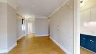 Located at 1222 SW Broadway in the heart of Portland, Oregon, this thoughtfully laid-out unit offers a well-organized single-floor plan comprising a living room, kitchen, bathroom, and two hallways. Light hardwood flooring runs throughout, lending warmth and continuity to each space.

The living room is an open, airy area highlighted by large French doors that invite natural light and frame views of the surrounding urban cityscape. A classic cast-iron radiator adds a charming architectural detail, complemented by elegant crown molding along the ceiling perimeter.

The kitchen is a standout feature, showcasing a striking two-tone cabinet design with deep navy lower cabinets and crisp white upper cabinets, accented by a white subway tile backsplash. Stainless steel appliances, including a range and over-the-range microwave, complete the functional and stylish cooking space. A window allows natural light to brighten the area.

The bathroom retains a classic aesthetic with white subway tile walls accented by teal tile trim, a soaking tub with shower, pedestal sink, and a frosted glass window for privacy and light.

The hallways connect the spaces efficiently, with track lighting overhead and clean white trim throughout. The unit's neutral palette, hardwood floors, and period-inspired details create a cohesive and inviting urban living environment.