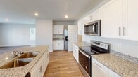 Located at 507 Satinwood Cir in Graniteville, South Carolina, this two-story home offers a clean, modern design with consistent wood-look flooring and neutral tones carried throughout both levels. The main floor features an open layout where the living area flows naturally toward the kitchen, which is outfitted with white shaker-style cabinetry, granite countertops, stainless steel appliances including a range, microwave, and refrigerator with ice dispenser, and a central island with a sink. Natural light filters in through windows fitted with white blinds, lending brightness to the space. A staircase with wood-tread steps connects the main floor to the upper level. Upstairs, the primary bedroom features a tray ceiling with a ceiling fan, creating an airy, elevated feel, and connects to a spacious en-suite bathroom with a dual-sink granite vanity and white cabinetry. An additional bathroom includes a granite vanity, shower-tub combo, and matching white finishes. A dedicated laundry room with full-size washer and dryer hookups and overhead shelving adds everyday convenience. The attached two-car garage offers generous space with an automatic opener. Throughout the home, recessed lighting and clean architectural lines contribute to a bright, well-maintained atmosphere.