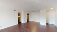 This single-floor residence at Plaza Square offers a well-organized layout designed for comfortable everyday living. The spacious living area is a standout feature, showcasing rich, dark hardwood-style flooring that extends throughout the main living spaces. A sliding glass door at one end of the room allows natural light to pour in while providing outdoor access, and a track lighting fixture adds focused illumination overhead. The textured ceiling adds subtle architectural character throughout.

The kitchen is efficiently designed with warm oak cabinetry offering generous upper and lower storage. Granite-toned laminate countertops provide ample workspace, complemented by a stainless steel sink, a stainless electric range, a dishwasher, and a full-size refrigerator. The kitchen connects openly to the living area, allowing for easy flow between spaces.

The bedroom is finished with plush carpeting for comfort and includes a window fitted with blinds, allowing for natural light and privacy. A ceiling-mounted light fixture provides overhead illumination.

The bathroom features a full tub and shower combination, a mirrored medicine cabinet, a wood-framed vanity with a single sink, and clean white finishes throughout, maintaining a bright and tidy atmosphere.