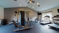 Located at 575 Sycamore Ln in Aurora, Ohio, this single-floor fitness center is designed to accommodate a comprehensive workout experience. The space is divided into two distinct exercise areas, each thoughtfully equipped and finished for functionality and comfort.

The primary workout room features vaulted ceilings with recessed lighting and a ceiling fan, creating an open and well-ventilated environment. Durable rubber flooring provides a safe, impact-resistant surface throughout. This area houses a multi-station cable strength machine, a rowing machine, an elliptical trainer, and two Spirit-brand treadmills. Wall-mounted flat-screen televisions are positioned for easy viewing during cardio sessions, and a window overlooking an outdoor pool area allows for natural light and a pleasant exterior view.

A secondary exercise room offers a more intimate setting with standard ceiling height, recessed lighting, and matching rubber flooring. This space includes an air resistance bike and a recumbent stationary bike, along with an additional wall-mounted television. A framed interior window connects visually to a hallway, enhancing the sense of openness. Exercise balls and additional accessories are also available, supporting stretching and functional fitness routines. Together, the two areas provide a well-rounded facility suited for both cardio and strength training.