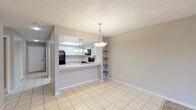 This single-floor residence offers a thoughtfully designed layout that balances functionality and comfort throughout. The kitchen is a standout feature, showcasing white upper cabinetry with frosted glass inserts, gray lower cabinets, granite-style countertops, a tray ceiling with recessed lighting, and a full suite of black appliances including a refrigerator, electric range, microwave, and dishwasher. Light tile flooring runs through the kitchen and flows into the adjacent dining area, which is highlighted by a stylish pendant light fixture and built-in corner shelving — a charming architectural detail that adds both character and practicality. The open living area transitions to wood-look flooring and features a ceiling fan, neutral walls, and a sliding glass door that opens to a private balcony with outdoor views. The bedrooms are carpeted and well-sized, each equipped with ceiling fans. The primary bedroom includes a dedicated en-suite bathroom with a vanity and walk-in shower, while a secondary bedroom offers a roomy closet with built-in shelving. A full guest bathroom with a tub-shower combination and tile flooring serves the remaining rooms. A dedicated in-unit laundry room with wire shelving and a full-size washer and dryer completes this practical and comfortable home.